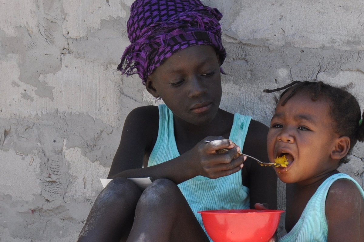 Isosisko syöttää ruokaa lusikalla pikkusiskolle Ambomaalla, Namibiassa.