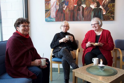 Kolme naista istuu kirkkokahveilla kahvikupit käsissään.